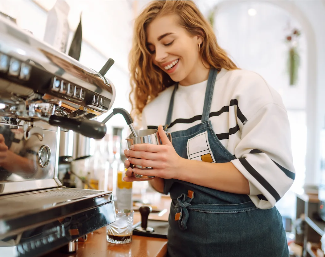 Female café barista preparing coffee while hospitality rostering software helps optimise staff scheduling.
